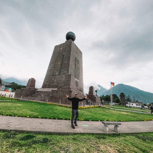 איש עומד מול מוניומנט של אמצע העולם אקוודור